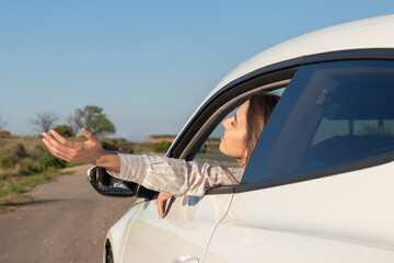 Woman with eyes closed leaning out of car window with arm outside enjoying the fresh breeze of nature in a road trip
