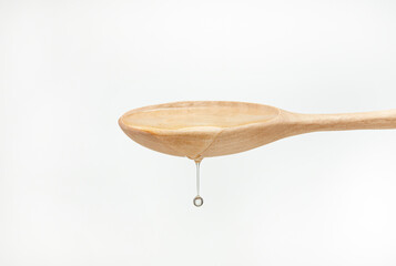Stream of oil pours with drop from a wooden spoon on a white background. Shallow depth of field