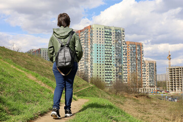 Woman looks at the new houses standing on green hill, urban landscape in spring. Building industry and real estate concept