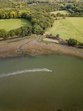 Aerial view of the River Hamble as a speed boat creates a wake in the water and passes woodland scene, Hamble, Southampton, United Kingdom.
