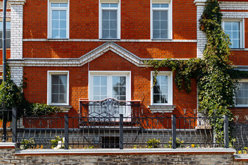Fototapeta na wymiar View of the beautiful facade of a red brick house with a vintage balcony and windows with climbing ivy.