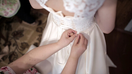 Fototapeta na wymiar Mother helps the bride to put on a wedding dress. Stock. Hands tie a corset of a wedding dress