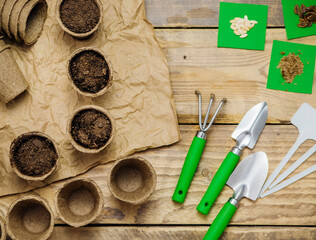 Top view of seeds and garden tools on a wooden background. Growing seedlings using peat cups.