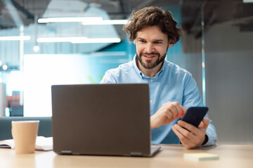 Portrait of smiling man using smartphone and pc at office