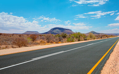 Fototapeta na wymiar Beautiful empty asphalt dirt road in desert plain with mountains in background - Namibia, Africa
