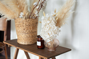 Cozy autumn decor room: on wooden table wicker basket with dried flowers, candle and vase with...