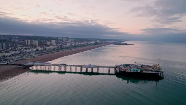 Aerial video drone flies over Brighton Pier, quiet town and calm sea at twilight, UK 