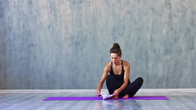 beautiful young woman of Caucasian ethnicity in sports black clothes leggings and a tank top is engaged in yoga in the studio with natural lighting on purple mats for gymnastics. Active lifestyle