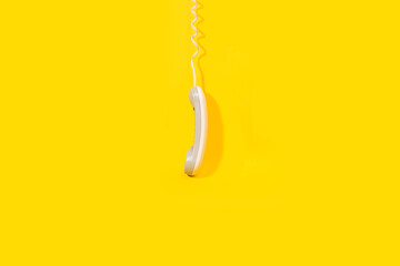 Tubo de teléfono con cable colgando sobre un fondo amarillo brillante liso y aislado. Vista de frente. Copy space - obrazy, fototapety, plakaty