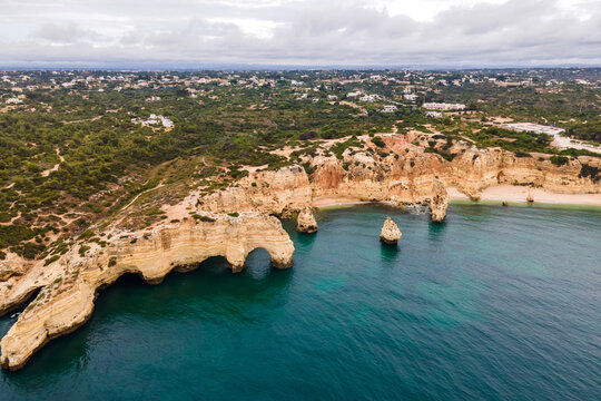 Aerial view of Praia da Marinha and Praia da Mesquita with natural arch at sunrise along the coastline in Lagoa, Faro, Algarve region, Portugal.