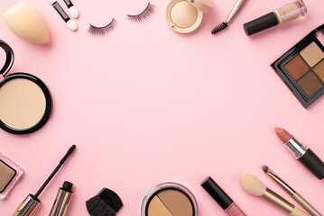 Top view photo of eyeshadow palette lipstick compact powder blush false eyelashes makeup brushes mascara lip gloss beauty blender nail polish on pastel pink background with blank space in the middle
