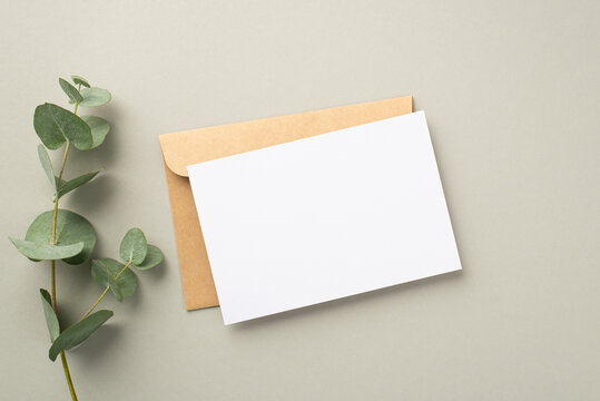 Business concept. Top view photo of paper card craft paper envelope and eucalyptus sprig on pastel grey background with blank space