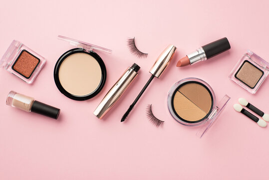 Make up concept. Top view photo of false eyelashes lipstick compact powder blush eyeshadow brushes nail polish and mascara on pastel pink background