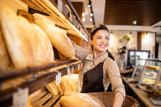 Deli worker arranging fresh pastries and bred in supermarket bakery department.