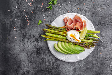 Salad of asparagus, avocado, poached egg and prosciutto, jamon, bacon. on black background. Keto...