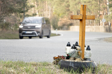 A roadside memorial cross with a candles commemorating the tragic death, on a background ride...