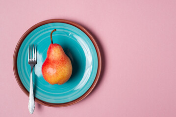 fresh red pear on a green plate with a fork on a pink background