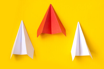 a red paper airplane and two white ones on a yellow background. The concept of leadership, teamwork and courage.