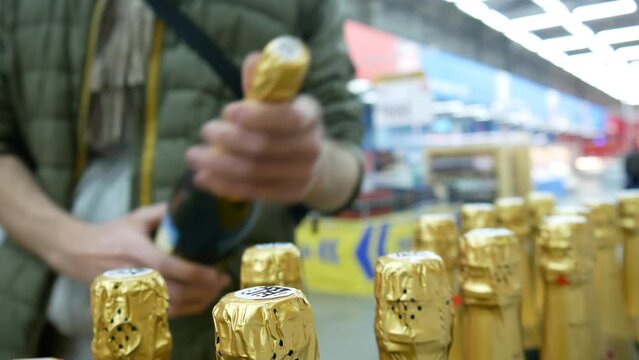 Close-up of many champagne bottles with gold foil caps in a store and a man takes one