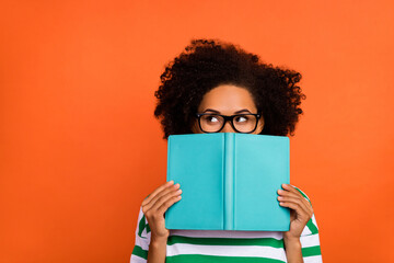 Portrait of attractive funny intellectual wavy-haired girl reading diary closing face copy space isolated on bright orange color background