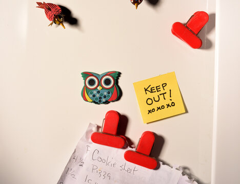 Closeup shot of a fridge door with magnets and a note saying keep out