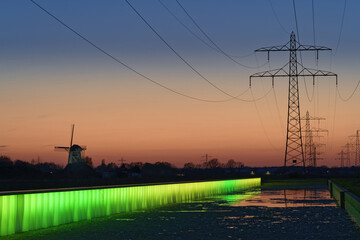 Scenic shot of electricity towers located behind a small water stream during the sunset