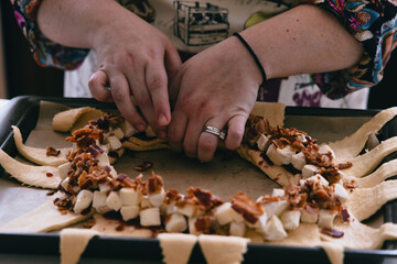 Closeup of female hands wrapping food in a round dough on a baking sheet