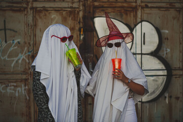 Funny image of two people in ghost costumes drinking from a cu