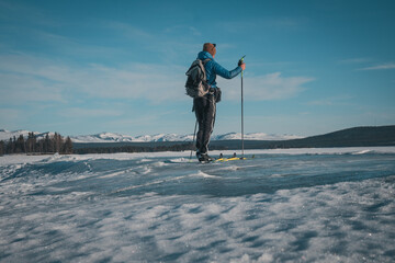 Young white man with skis and backpack and blue down jacket on frozen lake Storsjö with mountain view (onto Storådörren) close to Ljungdalen (Sweden). - obrazy, fototapety, plakaty
