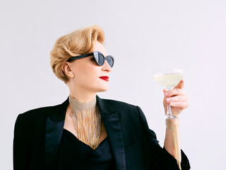 mature stylish elegant woman in tuxedo and sunglasses with glass of sparkling wine. Party,...