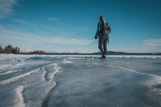 Young white man with skis and backpack and blue down jacket on frozen lake Storsjö with mountain view (onto Storådörren) close to Ljungdalen (Sweden).