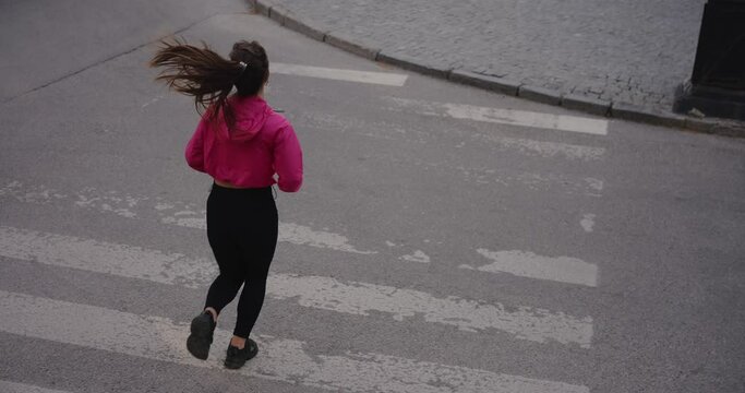 Sporty woman jogging in the city crossing road on a zabra, slow motion
