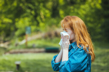 Woman with allergy symptom blowing nose. Attractive Woman Outdoors is Having Allergy. Woman Blowing Her Nose With Handkerchief In Public Parkf. Sick Young Woman With Seasonal Influenza - obrazy, fototapety, plakaty
