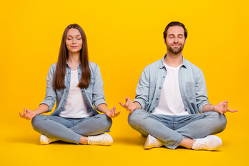 Portrait of attractive dreamy couple sitting meditating om zen isolated over bright yellow color background