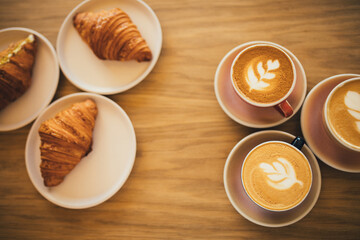 Freshly baked crusty croissants and coffee on wooden table.