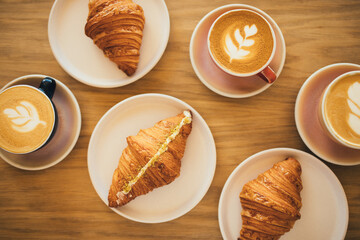 Freshly baked crusty croissants and coffee on wooden table.