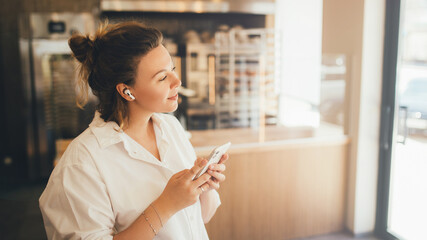 Young woman listening to music online using her smartphone and wireless earphones.