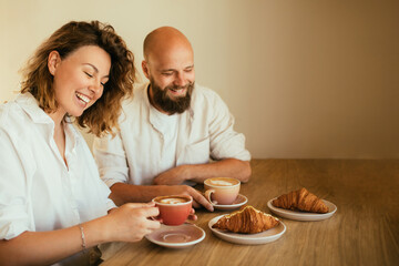 Happy couple in love drinking coffee with croissants, sitting in a coffee house.