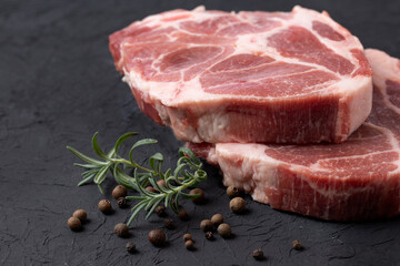 Steaks of raw marbled pork tenderloin on a black background with rosemary and peppercorns.