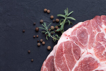 Steaks of raw marbled pork tenderloin on a black background with rosemary and peppercorns. Top view.