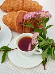 Two cup black tea with flowers and fresh croissants on the table against white background. Flat lay, spring breakfast conceptual composition