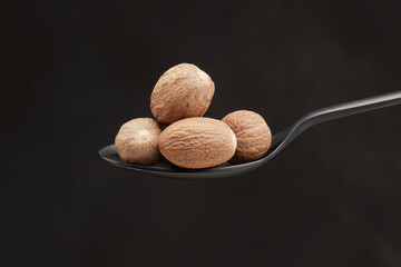 Pile of nutmegs in a  black spoon on a black background. Shallow depth of field
