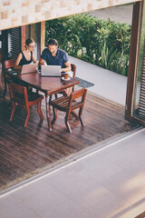 Coworking and freelance concept. Young  bearded man  and young woman working together on laptop computers while sitting on cafe terrace.