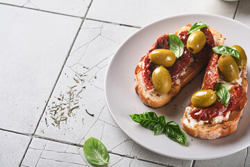 Bruschetta with sun dried tomatoes. Toast or sandwich with ricotta, sun dried tomatoes and Provence herbs with basil servered on a plate on a grey old cracked tile table. Top view banner menu recipe.