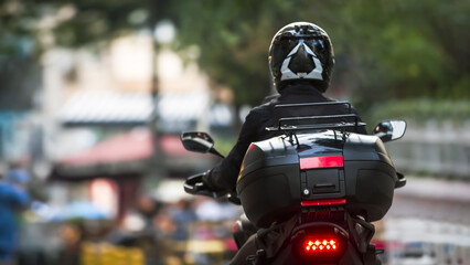 Back view of a courier on a motorcycle with suitcase on the back on a blurred street background