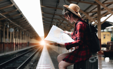 Young traveler woman looking on maps planning trip at train station. Summer and travel lifestyle concept - obrazy, fototapety, plakaty