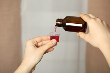 Woman pouring cough syrup into measuring cup on blurred background, closeup