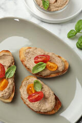 Slices of bread with delicious pate, tomatoes and basil on white marble table, flat lay