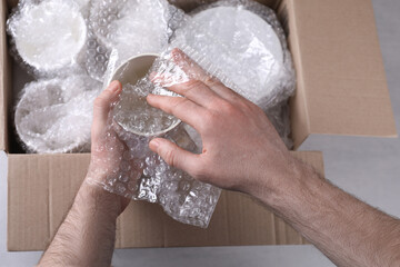 Man covering ceramic dishware with bubble wrap, closeup