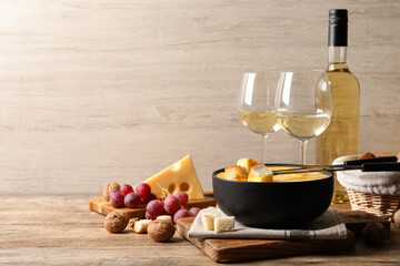 Tasty cheese fondue, snacks and wine on wooden table, space for text